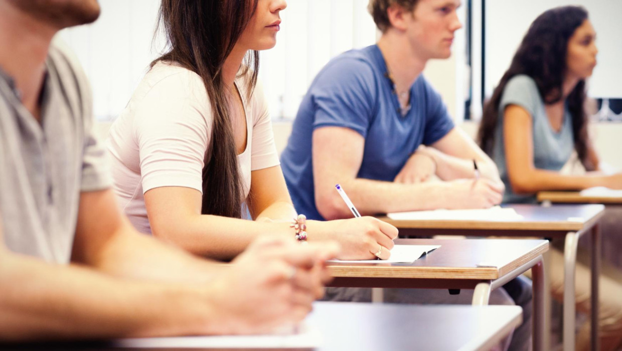 adultos jovenes estudiosos escuchando mientras estan sentados en el escritorio del aula